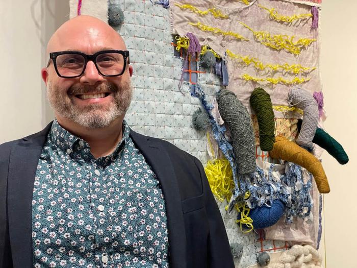 John Chaich, gay New York-based independent curator and founder of "Queer Threads," stands in front of "Secrets of Greenmont West, 2019" created by San Francisco Bay Area artist collaborative RoCoCo. Photo: Heather Cassell